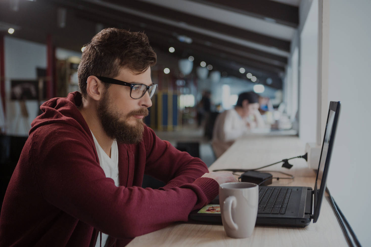Young serious concentrated man in glasses sitting in office and using laptop Young serious concentrated man in glasses sitting in office and using laptop